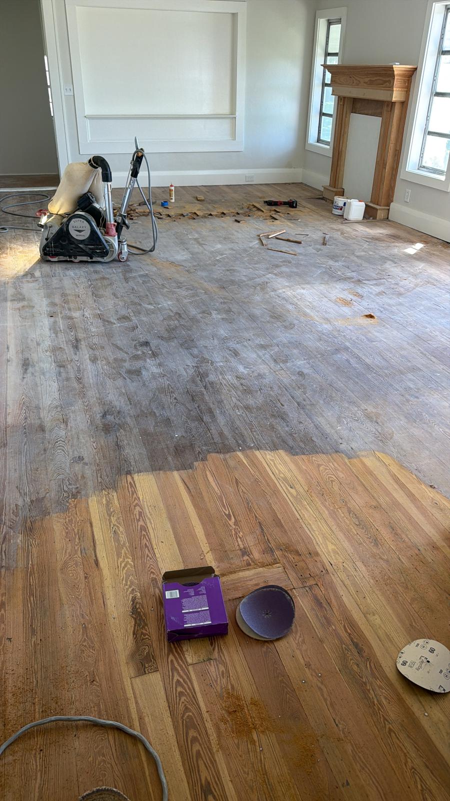 Professional drum sander mid-restoration in a Cape Coral home, with walls, windows and fireplace visible